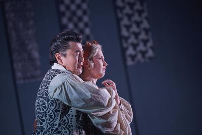 A Chinese man wraps his arms around a Caucasian woman from behind, both with emotionally distressed faces