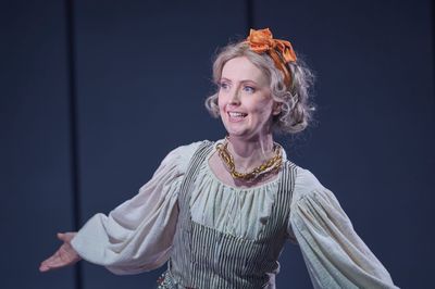 A Caucasian woman spreads her arms out wide as she sings