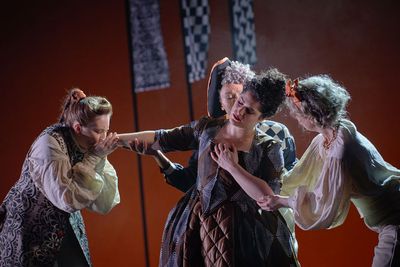 A woman has fainted, being held up by 2 women, and a third woman (who is dressed as a man) kisses her hand