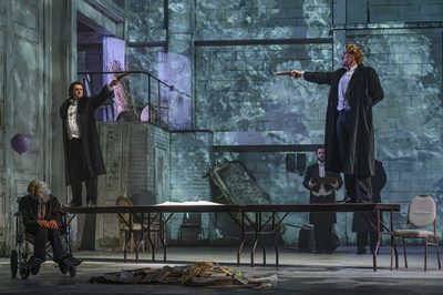 2 men stand on top of a long table, both with guns raised ready to shoot the other