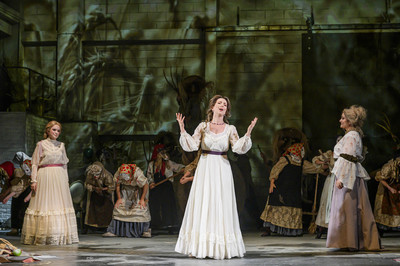 A woman sings with expressive hand gestures while 2 other women watch either side of her